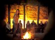 Mary-Ann performing to an audience around a glowing open fire inside a thatched hut