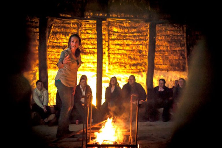 Mary-Ann performing to an audience around a glowing open fire inside a thatched hut
